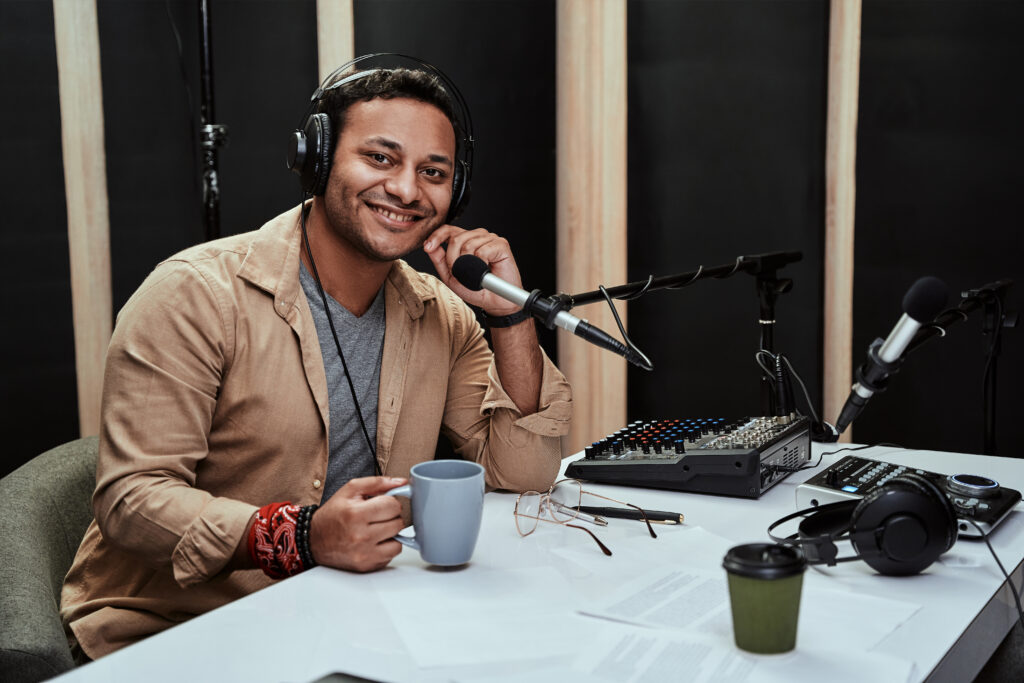 Portrait of happy young male radio host having a drink, smiling at camera while moderating
